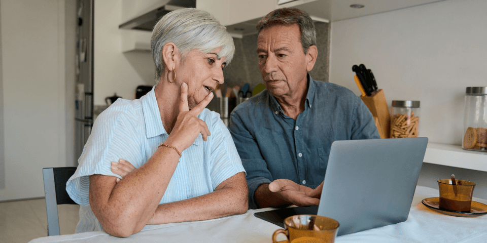Senior couple using a laptop at home, having breakfast and discussing finances